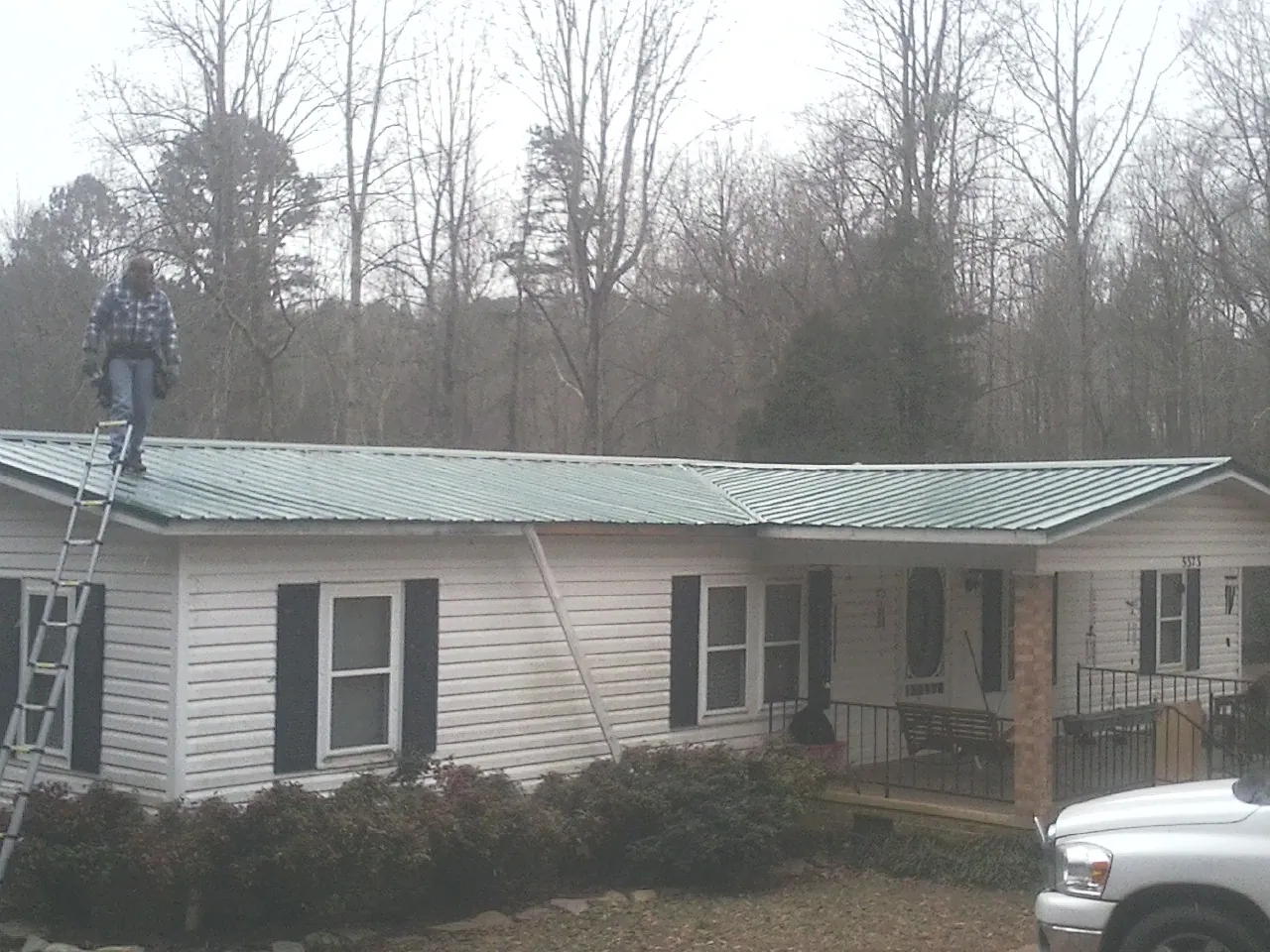 Worker on a ladder beside a new green metal roof on a ranch home in Sherman