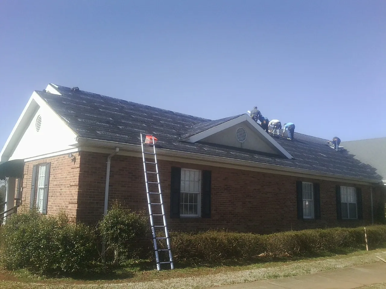 Crew tearing shingles off a brick ranch roof with a ladder set — Metal Roof Repair work by our crew in Sherman